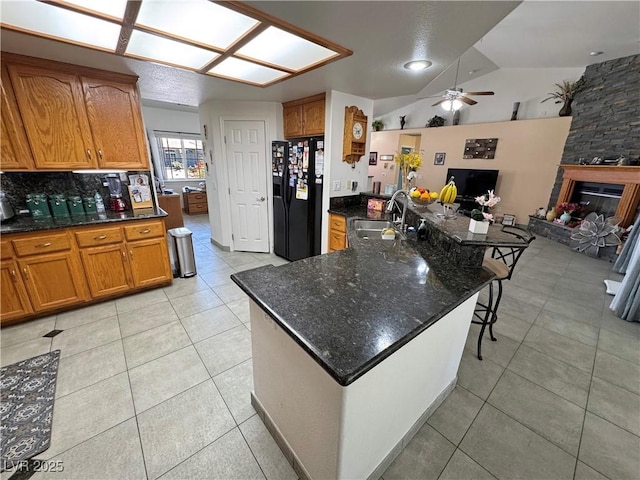 4910 Marywood Ct, Pahrump, NV 89061 - kitchen with black refrigerator with ice dispenser, brown cabinets, light tile patterned floors, vaulted ceiling, and ceiling fan