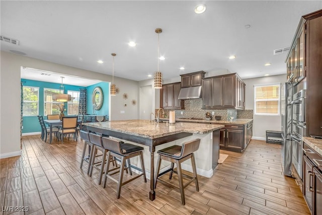 2154 Tortona St, Henderson, NV 89044 - kitchen with under cabinet range hood, light wood-style floors, dark brown cabinets, a kitchen bar, and light stone counters