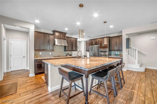 2154 Tortona St, Henderson, NV 89044 - kitchen with appliances with stainless steel finishes, under cabinet range hood, dark brown cabinetry, a breakfast bar, and light wood-style floors