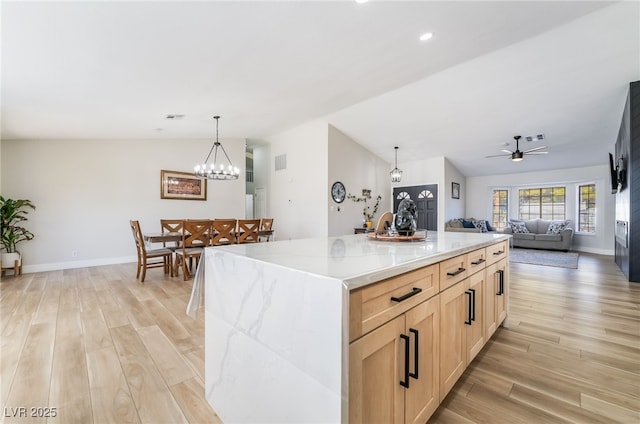 5570 Palm St, Las Vegas, NV 89120 - kitchen featuring light wood-style floors, lofted ceiling, light brown cabinetry, light stone counters, and hanging light fixtures