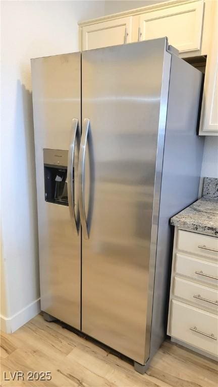 3930 Starfield Ln, Las Vegas, NV 89147 - kitchen view of stainless steel fridge with ice dispenser, light wood finished floors, light stone countertops, and white cabinets