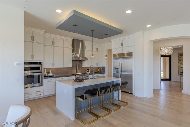 975 Amara Way, Henderson, NV 89052 - kitchen with stainless steel appliances, wall chimney range hood, a chandelier, light wood-style flooring, and white cabinets