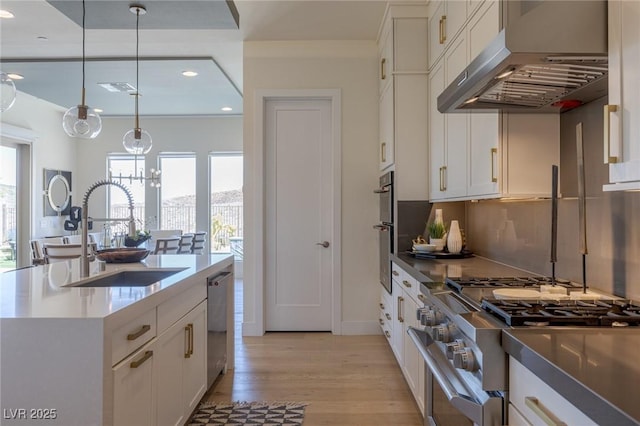 975 Amara Way, Henderson, NV 89052 - kitchen with under cabinet range hood, stainless steel appliances, light wood finished floors, white cabinets, and hanging light fixtures