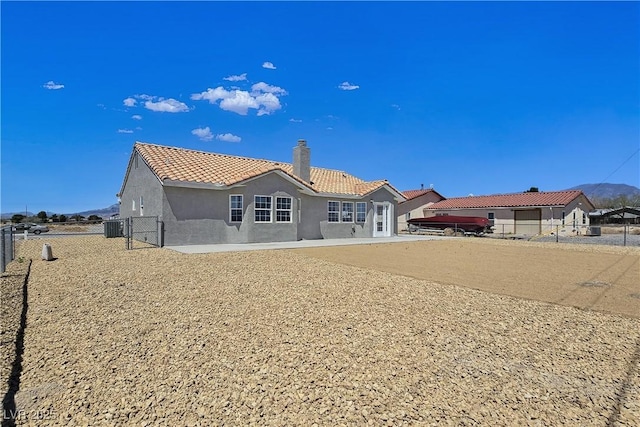 3326 Mount Charleston Dr, Pahrump, NV 89048 - back of house featuring a tiled roof, stucco siding, a fenced backyard, a chimney, and a gate
