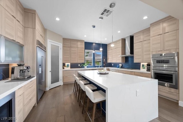 6804 Regency Stone Way, Las Vegas, NV 89148 - kitchen featuring light brown cabinets, wall chimney range hood, stainless steel appliances, modern cabinets, and a breakfast bar