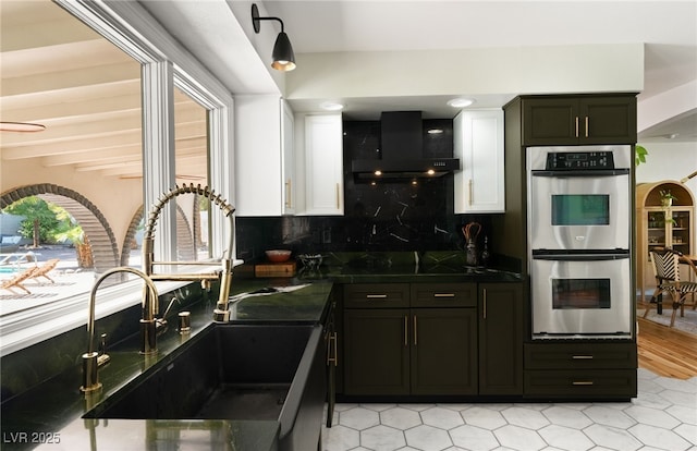 200 Stonewood Ct, Las Vegas, NV 89107 - kitchen featuring stainless steel double oven, wall chimney range hood, dark countertops, and white cabinetry