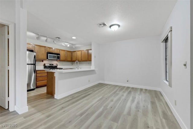 2627 S Durango Dr Unit 201, Las Vegas, NV 89117 - kitchen featuring stainless steel appliances, brown cabinetry, a peninsula, light wood finished floors, and light countertops