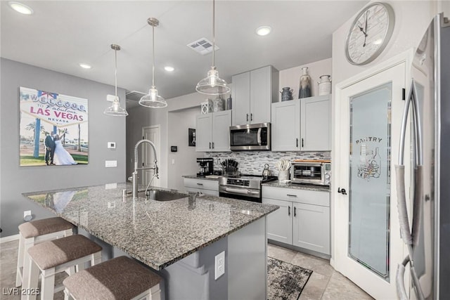 146 E Hawk Ave, Pahrump, NV 89060 - kitchen with appliances with stainless steel finishes, a kitchen breakfast bar, decorative backsplash, a kitchen island with sink, and light stone countertops