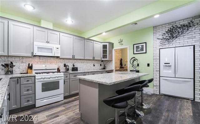 2253 Van Gogh Dr, Henderson, NV 89074 - kitchen with white appliances, gray cabinets, dark wood-style flooring, a kitchen breakfast bar, and decorative backsplash