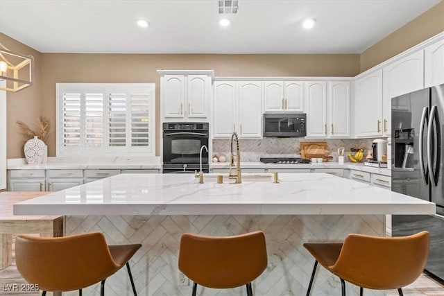 8929 Monte Oro Dr, Las Vegas, NV 89131 - kitchen with appliances with stainless steel finishes, white cabinetry, light stone counters, an island with sink, and a kitchen bar