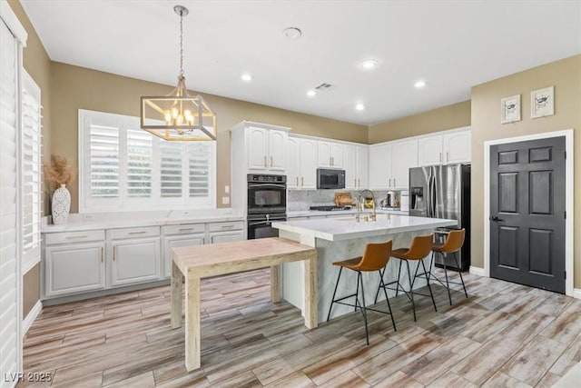 8929 Monte Oro Dr, Las Vegas, NV 89131 - kitchen with black appliances, white cabinets, light wood-style flooring, light countertops, and a chandelier
