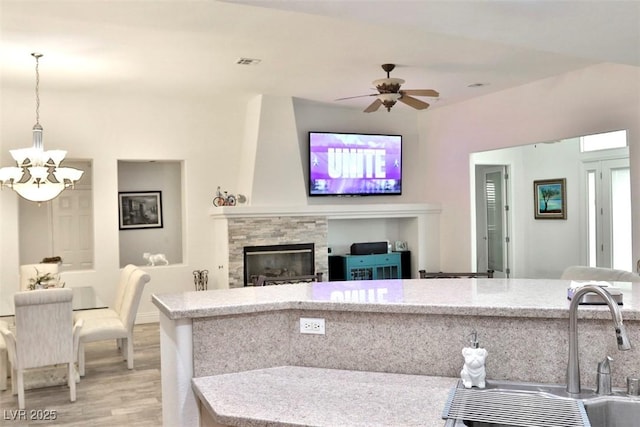 11240 Romette Ct, Las Vegas, NV 89141 - kitchen with a chandelier, light wood-style floors, hanging light fixtures, a stone fireplace, and ceiling fan