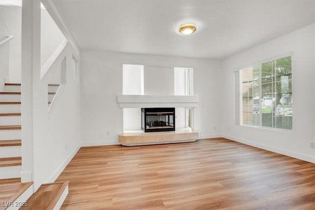 9824 Babys Breath Ct, Las Vegas, NV 89183 - unfurnished living room with stairway, light wood-style flooring, and a glass covered fireplace