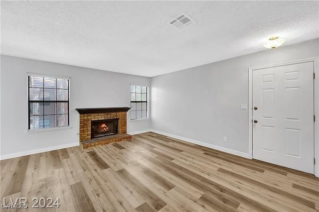 5576 W Rochelle Ave Unit 9C, Las Vegas, NV 89103 - unfurnished living room featuring a textured ceiling, light wood-type flooring, and a brick fireplace