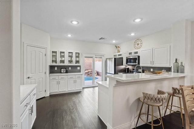 8325 Winterchase Pl, Las Vegas, NV 89143 - kitchen with appliances with stainless steel finishes, a breakfast bar area, a peninsula, white cabinets, and glass insert cabinets