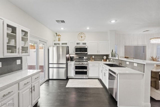 8325 Winterchase Pl, Las Vegas, NV 89143 - kitchen featuring appliances with stainless steel finishes, a peninsula, tasteful backsplash, light countertops, and glass insert cabinets