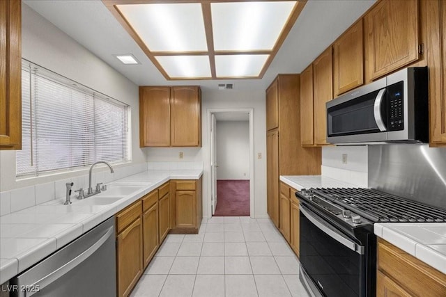 2344 Valleywood St, Henderson, NV 89014 - kitchen featuring appliances with stainless steel finishes, tile countertops, light tile patterned floors, and brown cabinets