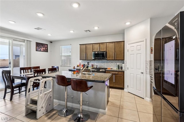 5246 Belmont Mill Ct, Las Vegas, NV 89122 - kitchen featuring stainless steel microwave, black refrigerator, stove, backsplash, and a breakfast bar area