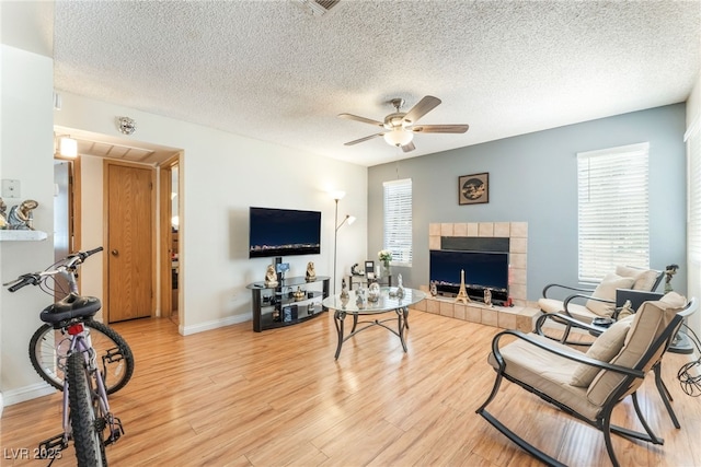 2666 Aarondavid Dr, Las Vegas, NV 89121 - living room featuring a ceiling fan, a tiled fireplace, a textured ceiling, and light wood-style flooring