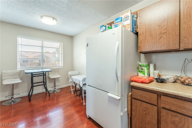 2666 Aarondavid Dr, Las Vegas, NV 89121 - kitchen featuring freestanding refrigerator, wood finished floors, light countertops, a textured ceiling, and brown cabinetry