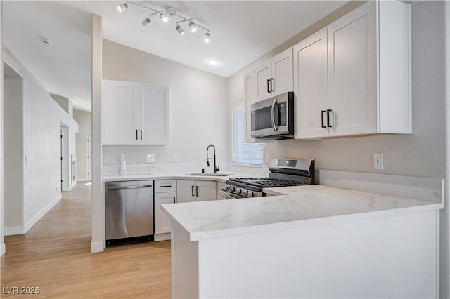 1005 Transom Dr, Las Vegas, NV 89128 - kitchen featuring appliances with stainless steel finishes, light wood finished floors, light stone counters, vaulted ceiling, and a peninsula