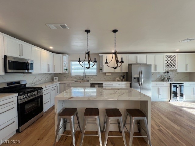 2712 Rialto Rd, Las Vegas, NV 89108 - kitchen with appliances with stainless steel finishes, wine cooler, a chandelier, light wood-type flooring, and decorative backsplash