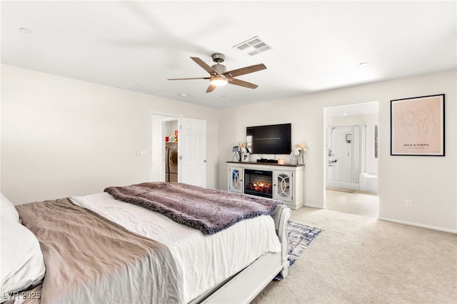 10940 Oregano Ave, Las Vegas, NV 89166 - bedroom featuring light colored carpet, washer / dryer, ensuite bathroom, a glass covered fireplace, and a ceiling fan