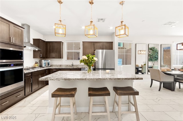 10940 Oregano Ave, Las Vegas, NV 89166 - kitchen featuring stainless steel appliances, wall chimney exhaust hood, light marble finish floors, a breakfast bar, and recessed lighting