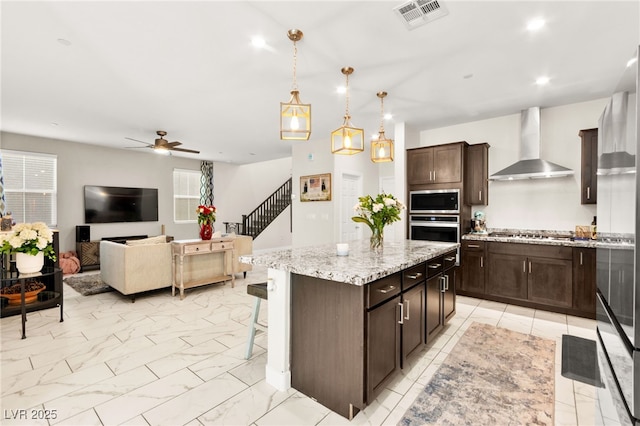 10940 Oregano Ave, Las Vegas, NV 89166 - kitchen with wall chimney range hood, stainless steel appliances, ceiling fan, a center island, and dark brown cabinets