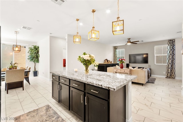 10940 Oregano Ave, Las Vegas, NV 89166 - kitchen featuring light marble finish floors, a ceiling fan, hanging light fixtures, light stone counters, and a center island