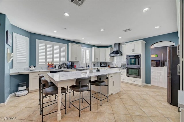 11417 Rock Cove Way, Las Vegas, NV 89141 - kitchen featuring appliances with stainless steel finishes, wall chimney exhaust hood, white cabinets, light stone countertops, and a kitchen bar