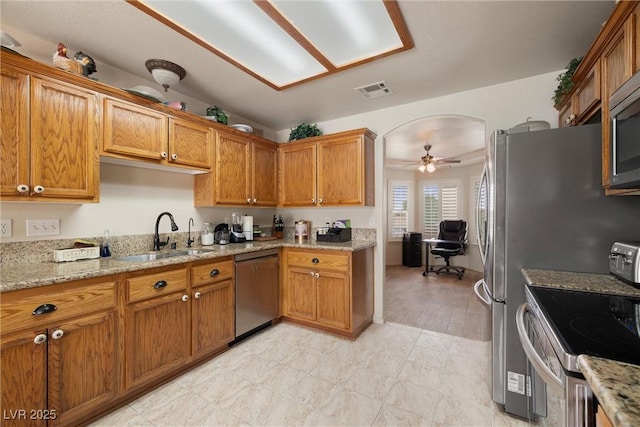 180 W Wilson Rd, Pahrump, NV 89048 - kitchen with appliances with stainless steel finishes, brown cabinetry, ceiling fan, and light stone counters