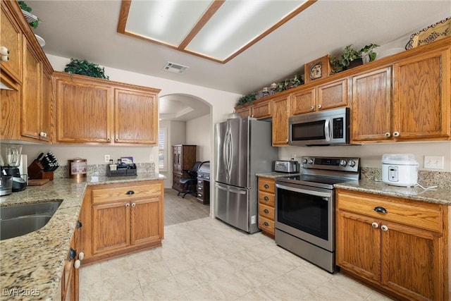 180 W Wilson Rd, Pahrump, NV 89048 - kitchen featuring stainless steel appliances, arched walkways, light stone counters, and brown cabinetry