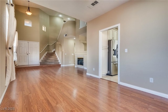 2245 Juniper Berry Dr, Las Vegas, NV 89134 - unfurnished living room featuring a towering ceiling, light wood finished floors, stairway, and a glass covered fireplace