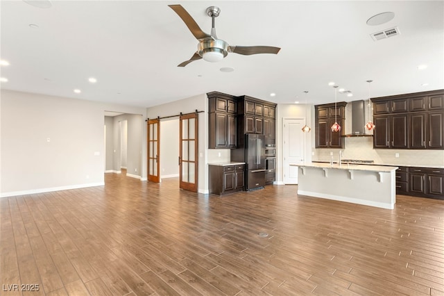 2116 Canvas Edge Dr, Henderson, NV 89044 - kitchen featuring wall chimney exhaust hood, open floor plan, light countertops, a ceiling fan, and a barn door