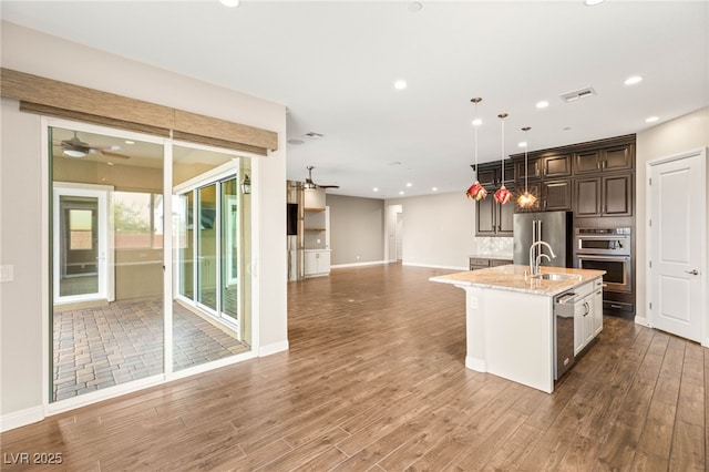 2116 Canvas Edge Dr, Henderson, NV 89044 - kitchen with a ceiling fan, appliances with stainless steel finishes, open floor plan, wood finished floors, and light stone countertops