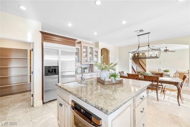2477 Adobe Wells Dr, Logandale, NV 89021 - kitchen featuring stainless steel appliances, ceiling fan, light stone counters, an island with sink, and glass insert cabinets