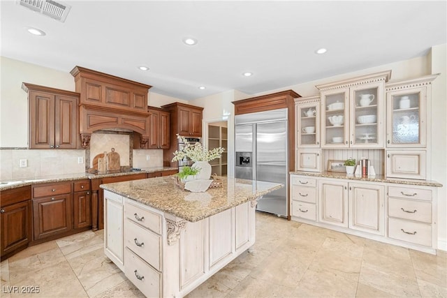 2477 Adobe Wells Dr, Logandale, NV 89021 - kitchen with built in refrigerator, tasteful backsplash, a kitchen island, glass insert cabinets, and light stone countertops