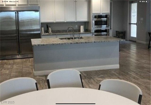 1860 Moonbow Falls St, Henderson, NV 89044 - kitchen with appliances with stainless steel finishes, light stone countertops, white cabinets, dark wood-type flooring, and a kitchen island with sink