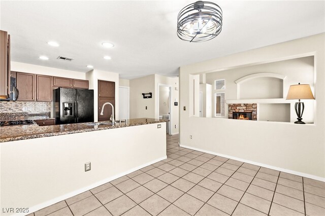 6044 Seneca Springs St, Las Vegas, NV 89130 - kitchen featuring black fridge, a fireplace, a peninsula, backsplash, and dark stone countertops