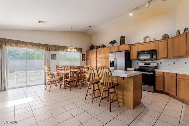 8840 Spinning Wheel Ave, Las Vegas, NV 89143 - kitchen featuring stainless steel appliances, vaulted ceiling, tile counters, light tile patterned floors, and a center island