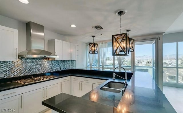 4575 Dean Martin Dr Unit 406, Las Vegas, NV 89103 - kitchen with wall chimney exhaust hood, stainless steel gas stovetop, decorative backsplash, white cabinetry, and decorative light fixtures