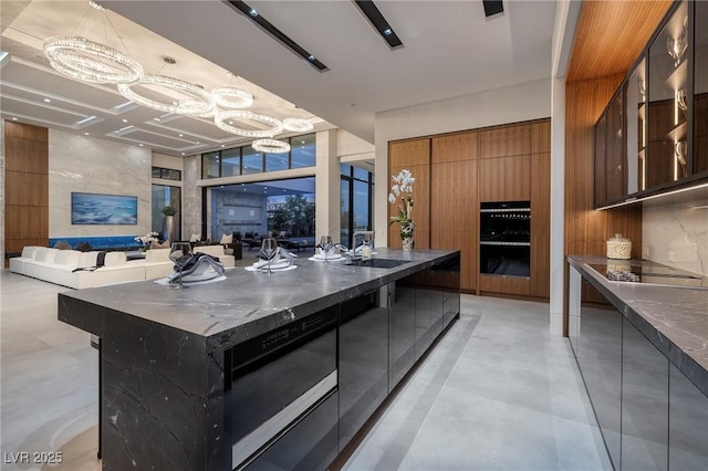 10891 Stardust Dr, Las Vegas, NV 89135 - kitchen with modern cabinets, a chandelier, black appliances, brown cabinets, and expansive windows