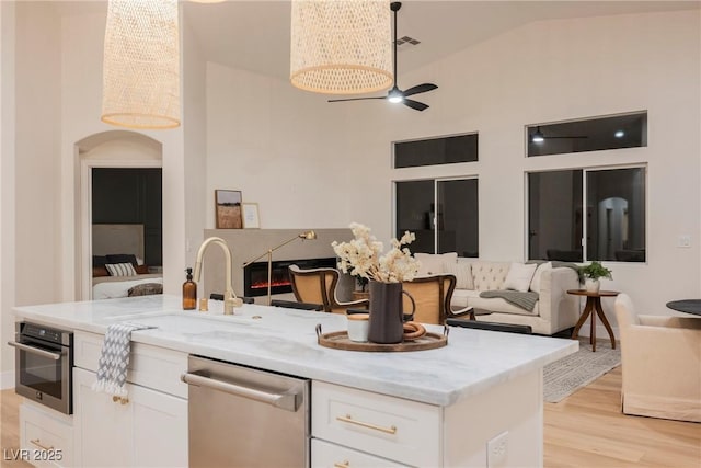 4065 Genoa Dr, Las Vegas, NV 89141 - kitchen with stainless steel appliances, open floor plan, white cabinetry, light wood-style floors, and light stone countertops