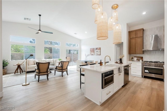 4065 Genoa Dr, Las Vegas, NV 89141 - kitchen featuring wall chimney range hood, stainless steel appliances, plenty of natural light, light wood-style floors, and vaulted ceiling