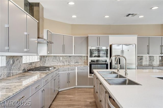 8113 Gothic Ave, Las Vegas, NV 89117 - kitchen featuring appliances with stainless steel finishes, gray cabinets, wall chimney exhaust hood, decorative backsplash, and light wood-style flooring