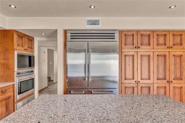 7045 Edna Ave, Las Vegas, NV 89117 - kitchen featuring built in appliances, brown cabinetry, light stone countertops, and recessed lighting