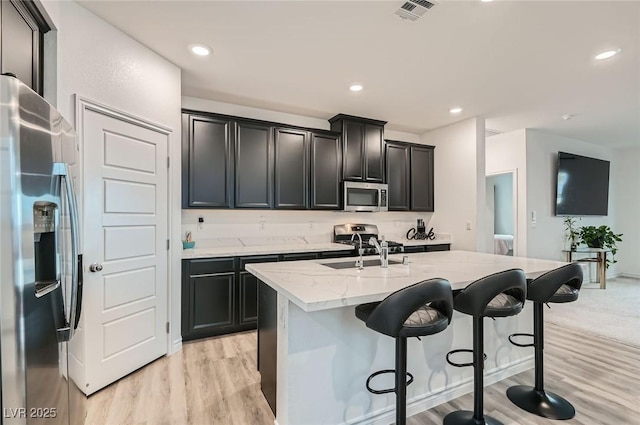 2821 Gaffer Film St, Las Vegas, NV 89156 - kitchen with appliances with stainless steel finishes, light stone countertops, a kitchen island with sink, light wood-type flooring, and a kitchen breakfast bar