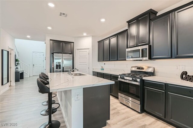 2821 Gaffer Film St, Las Vegas, NV 89156 - kitchen with appliances with stainless steel finishes, light wood-type flooring, light stone counters, an island with sink, and a kitchen bar