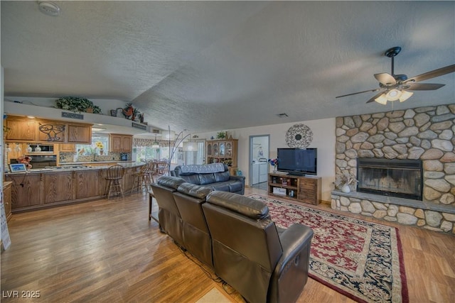 2910 Sunset St, Pahrump, NV 89060 - living area featuring a textured ceiling, lofted ceiling, light wood-style floors, a ceiling fan, and a stone fireplace
